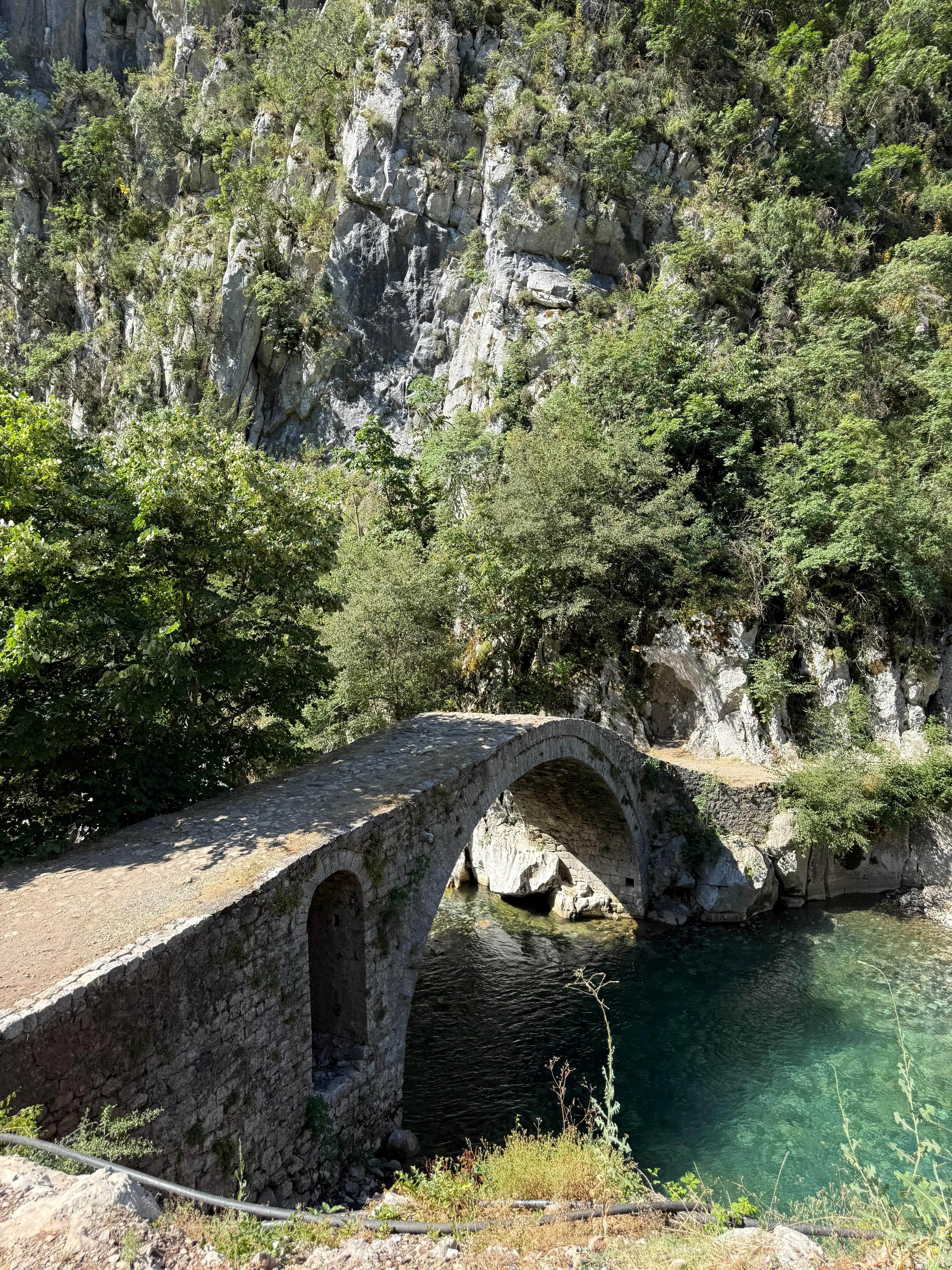 Close-up of an old stone arch bridge spanning turquoise water in Albania